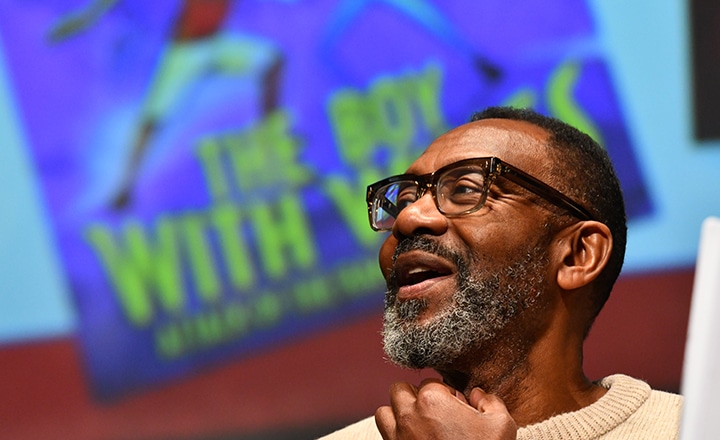 headshot of Lenny Henry speaking, with his book cover behind him