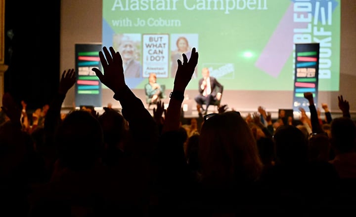 Silhouette hands in the air in front of the stage, with Alastair Campbell on stage