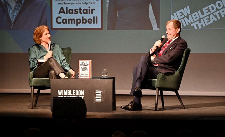Alastair Campbell on stage with an interviewer, talking about his book But What Can I Do?