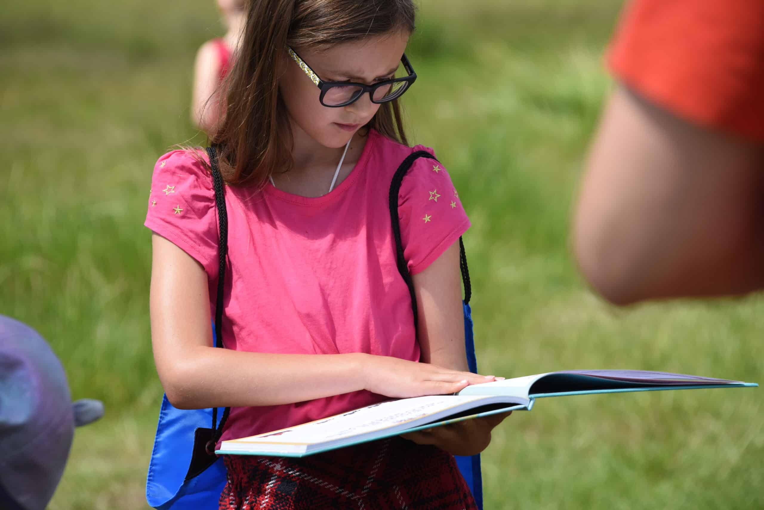 Young girl wearing glasses reading a book outdoors