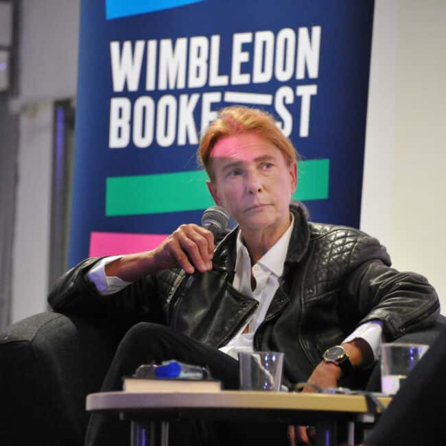 Lionel Shriver holding a microphone and wearing a leather jacket