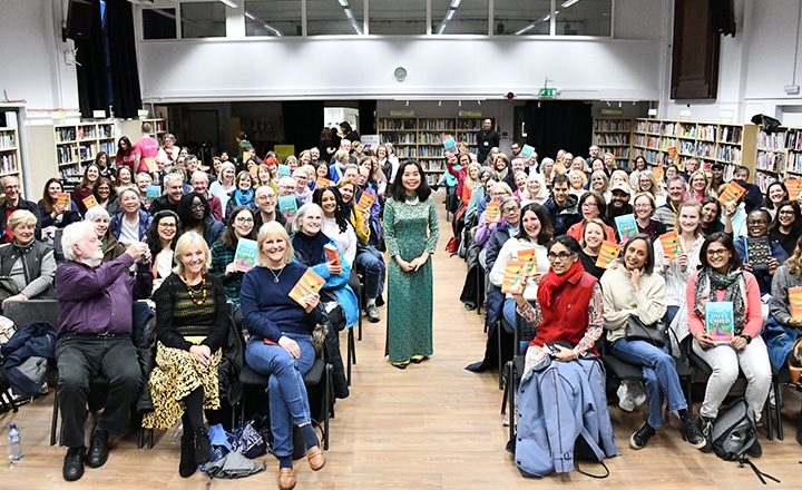 A large audience surrounding Nguyen Phan Que Mai smiling and holding books