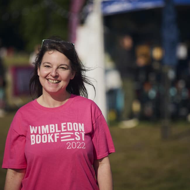 A Staff member in a Wimbledon Book Fest pink T-shirt smiling into the camera