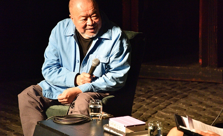 Author Ai WeiWei sat on a chair smiling into a microphone