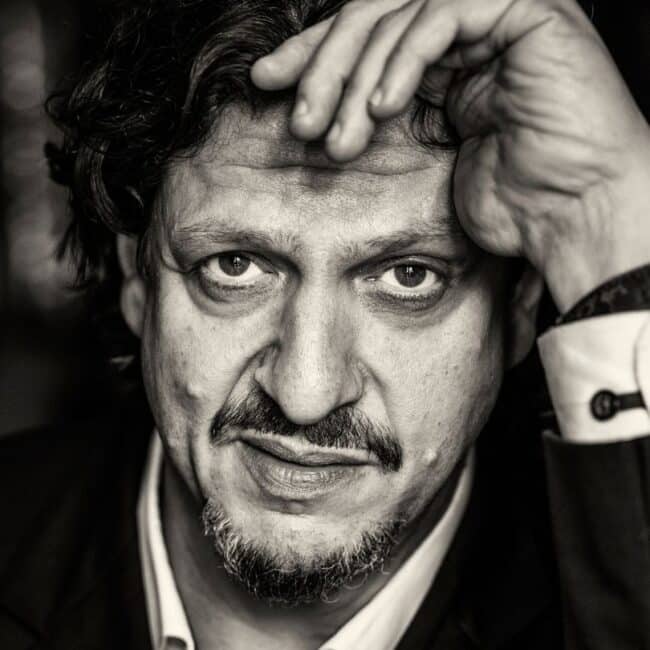 Jay Rayner speaking on stage at Wimbledon BookFest, holding a microphone and engaging with the audience.